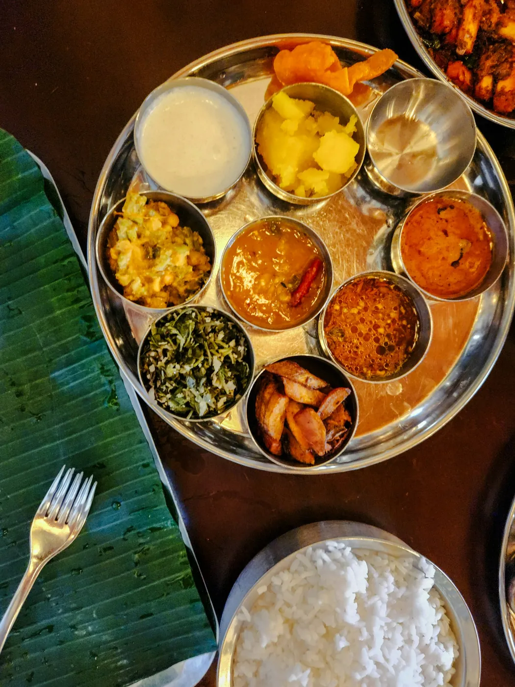 Overhead thali on a banana leaf with nine katoris, rice and a fork