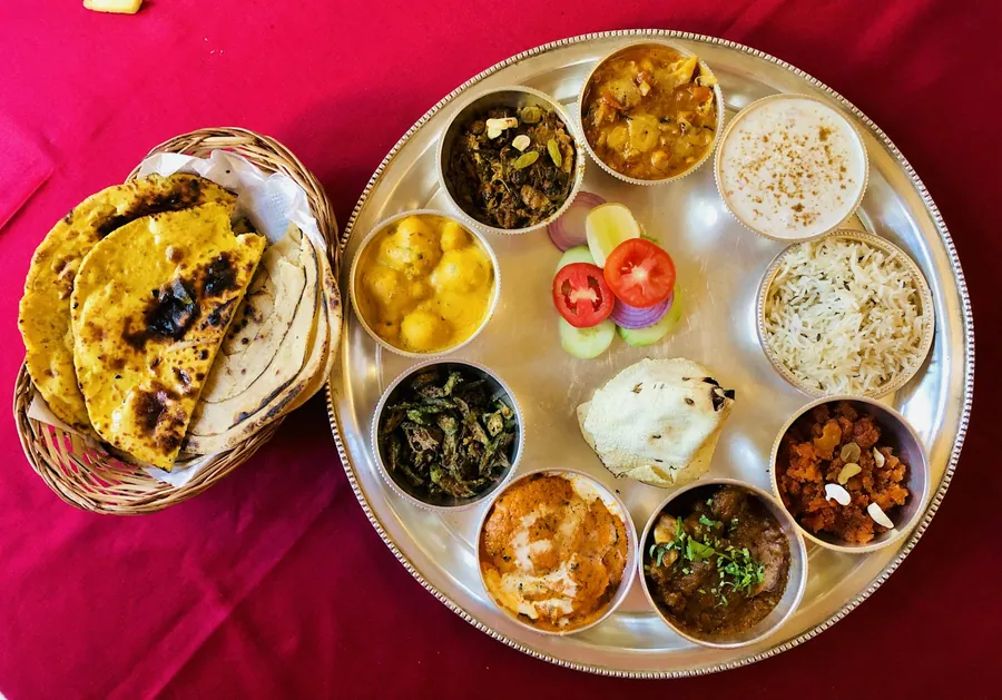 Round thali with curries, raita and salad, next to a basket of roti